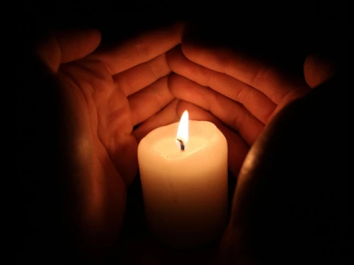 Bougie allumée dans le noir et dont la flamme est délicatement protégée par deux mains qui l'entoure