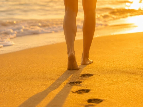 gros plan sur le bas des jambes d'une personne marchant sur la plage, pieds nus dans le sable, au bord de l'eau